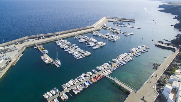 An aerial view of a marina with numerous boats docked, a pier, and a coastal landscape. - Apartments Agua Marina (Tías)