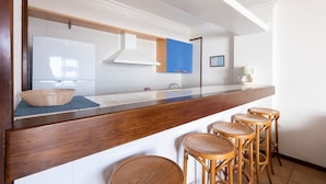 A modern kitchen with white cabinets, a wooden countertop, and a built-in stove. There are four wooden stools at the counter. - Apartments Agua Marina (Tías)