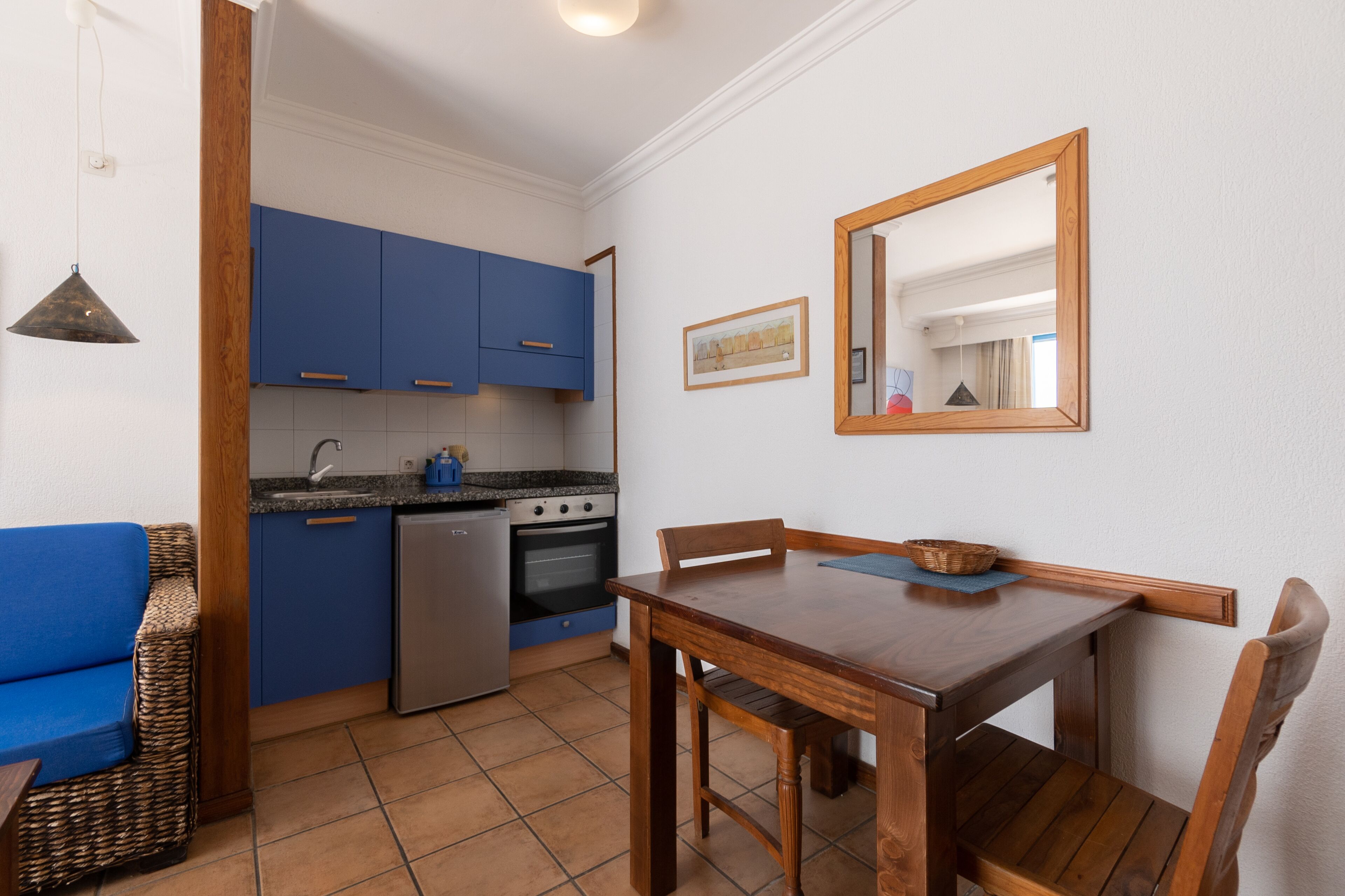 Una cocina compacta con armarios azules, una mesa de comedor y una silla de madera.