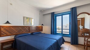 A hotel room with two beds, a wooden headboard, a desk, a chair, a window with curtains, and a painting on the wall. - Apartments Agua Marina (Tías)