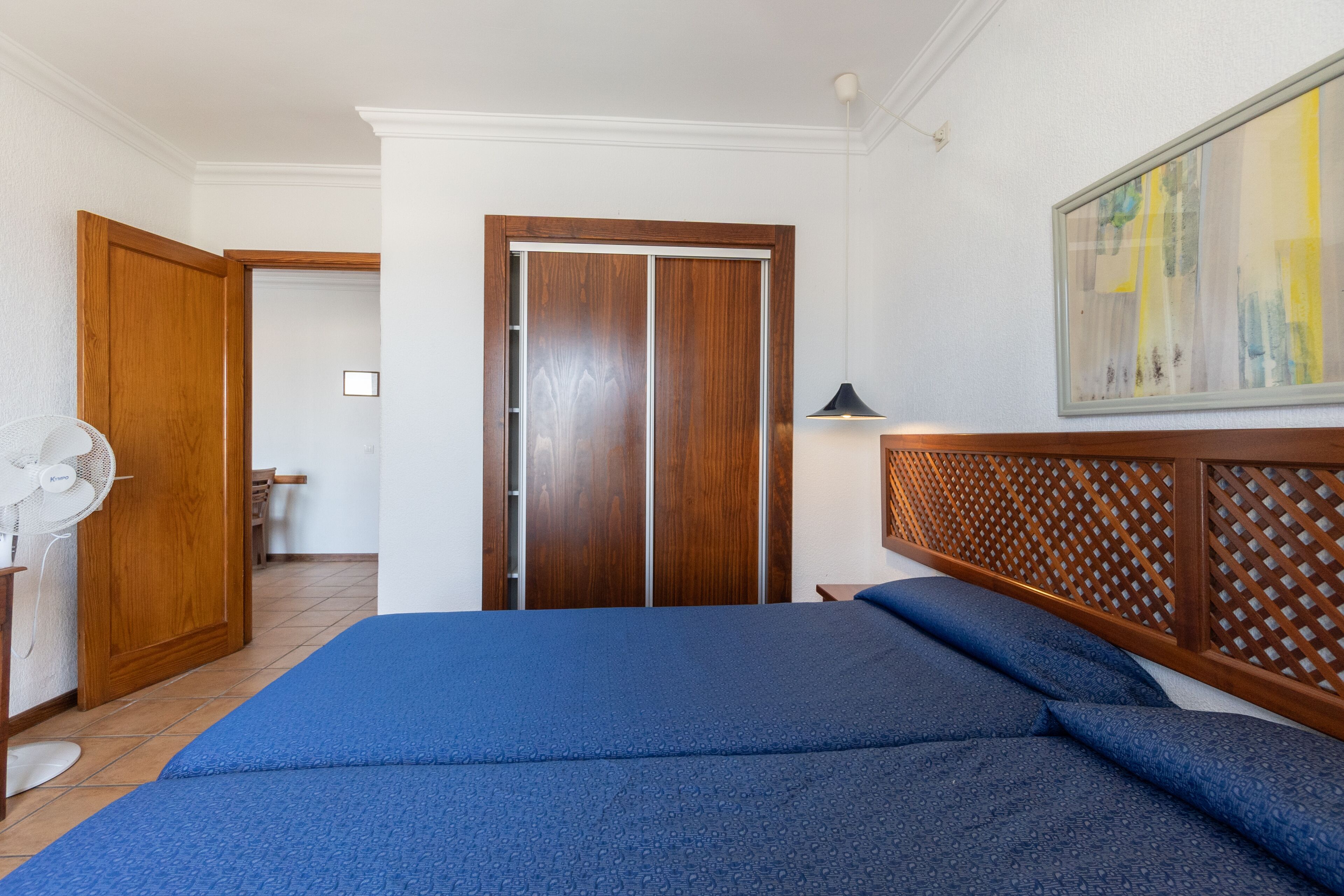 A bedroom with a bed, wooden wardrobe, and a fan.