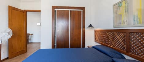 A bedroom with a bed, wooden wardrobe, and a fan.