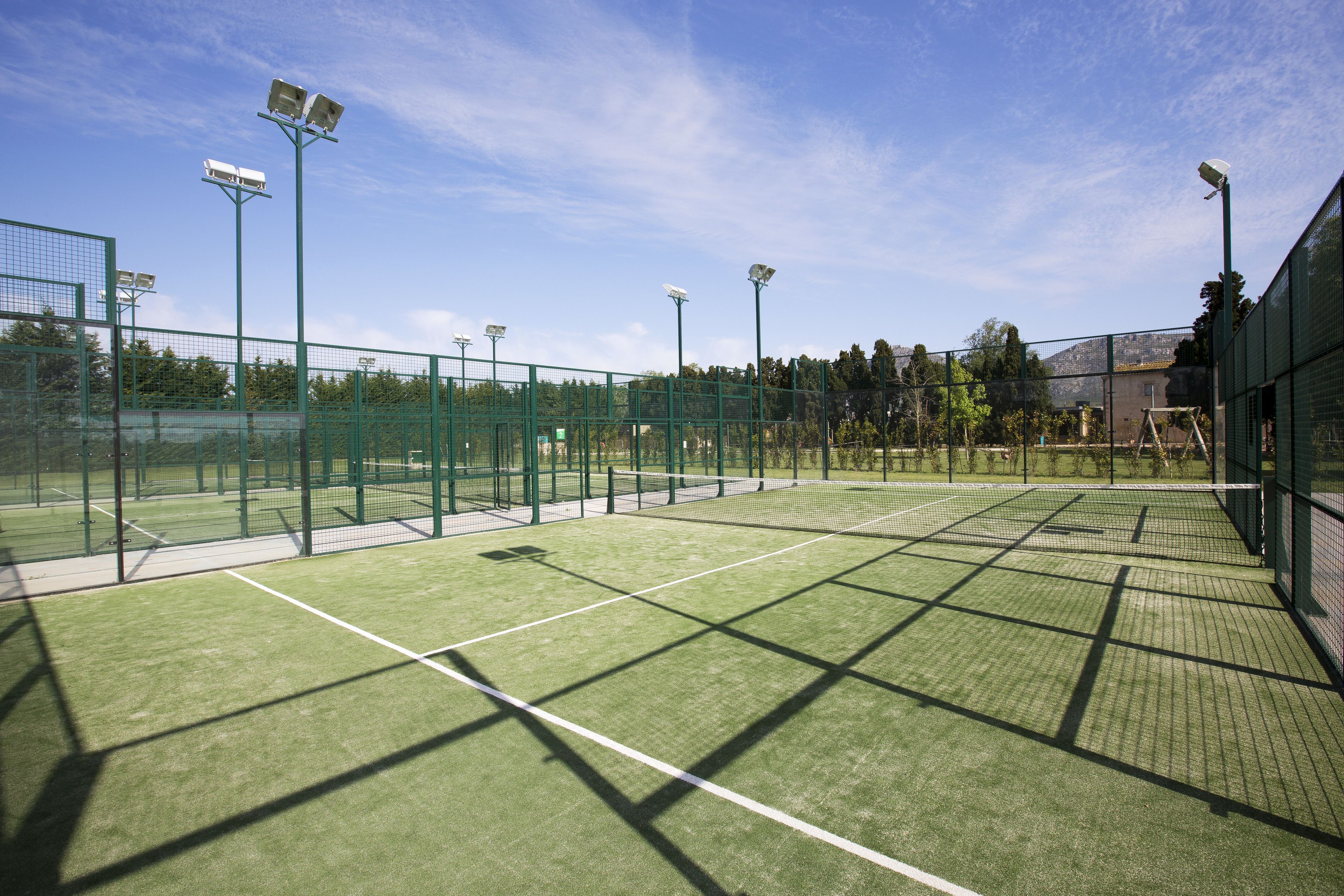 Canchas de tenis múltiples, rodeadas por una cerca verde, y equipadas con iluminación artificial.