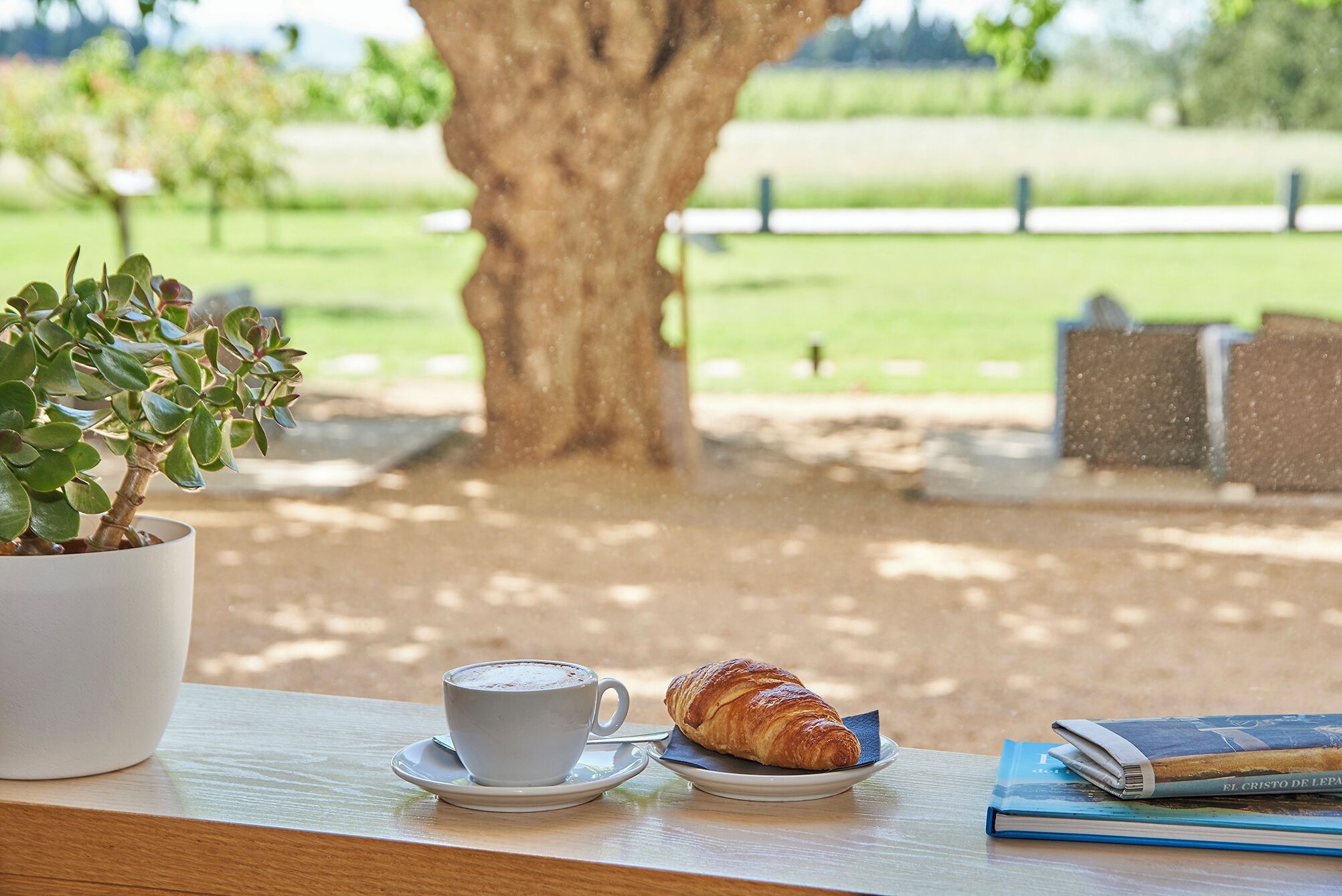 A table with a cup of coffee, a croissant, and a book.