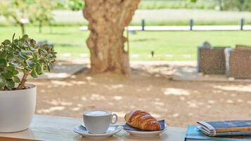 A table with a cup of coffee, a croissant, and a book.
