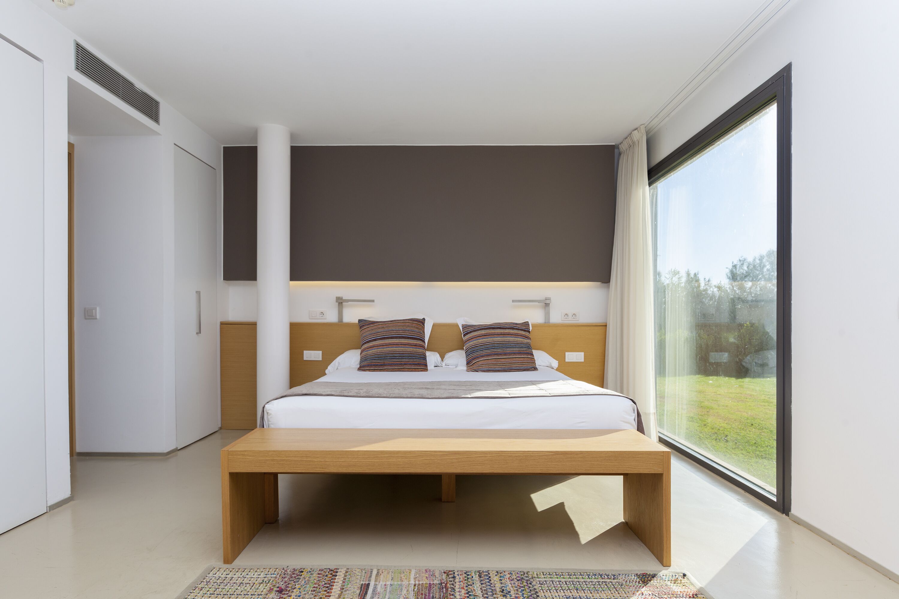 Un dormitorio moderno con una cama grande, un cabecero de madera y un amplio ventanal con vistas al exterior.