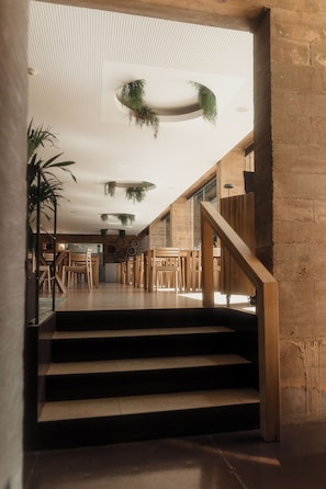 A modern interior with a staircase leading to a dining area, featuring wooden furniture and hanging plants.