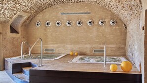 Uma área de spa com parede de pedra, várias banheiras de hidromassagem e um conjunto de degraus que levam a um patamar.