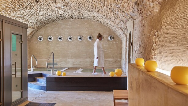 Um quarto de spa com parede de pedra, uma banheira e um banco de madeira.