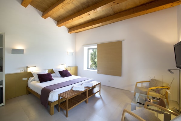 A modern bedroom with a wooden bed, a bench, a glass table, and a TV. - URH - Hotel Moli del Mig (Torroella de Montgrí)