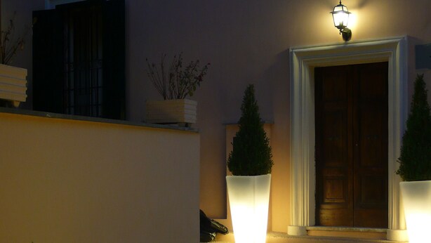A well-lit entrance with a door, two large illuminated spheres, and potted plants. - Locanda delle Corse (Rome)