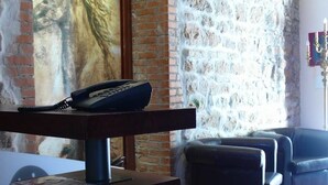 A room with a stone wall, a wooden table with a telephone, and two black leather sofas. - Locanda delle Corse (Rome)