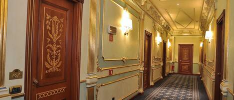 A grand hallway with ornate wood paneling, a patterned carpet, and wall sconces.
