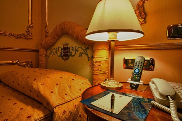 A hotel room with a bed, a bedside lamp, a telephone, and a desk with a pen and paper.