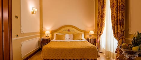 A hotel room with a large bed, two bedside tables, a chandelier, and a fruit bowl on a side table.