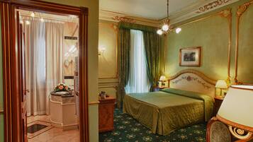 Una habitación de hotel con cama, mesita de noche, espejo, ventana con cortinas, puerta y baño con lavabo y espejo.