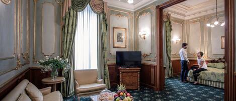 A room with a sofa, a coffee table with fruit, a television, and a bed.