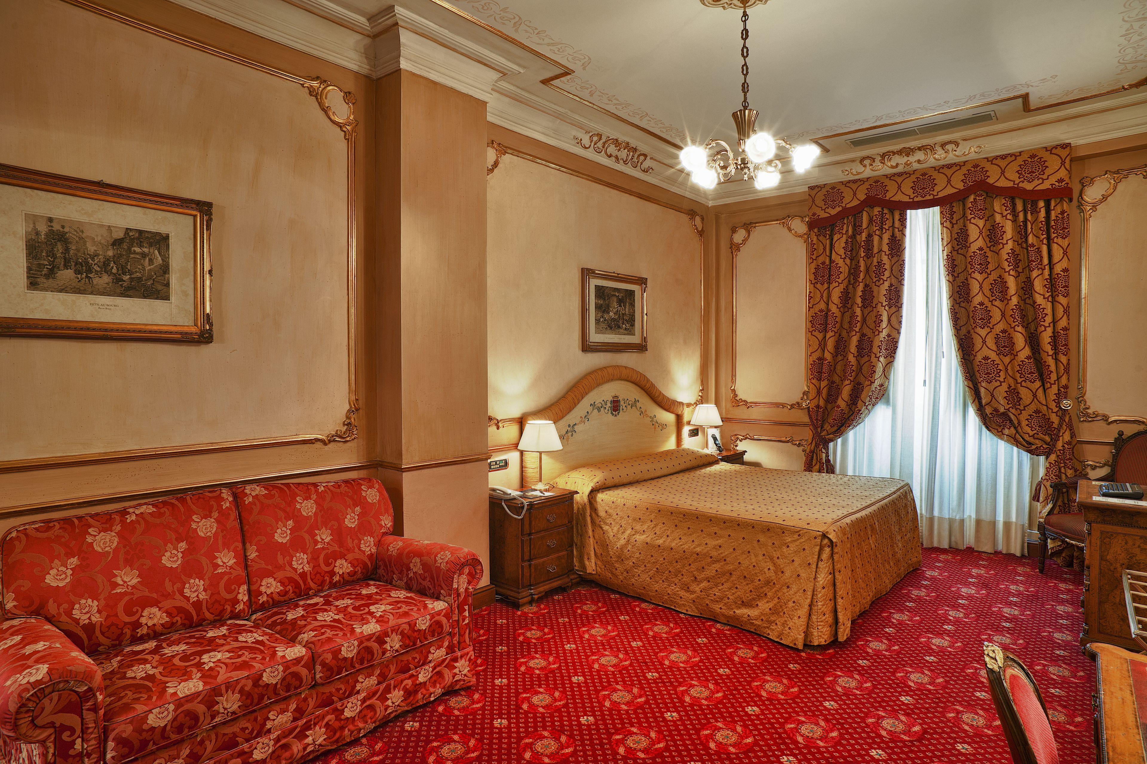 A hotel room with a bed, a sofa, a nightstand, and a desk.