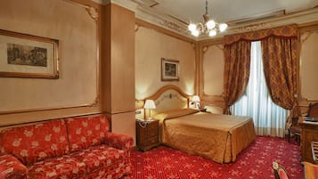 A hotel room with a bed, a sofa, a nightstand, and a desk.