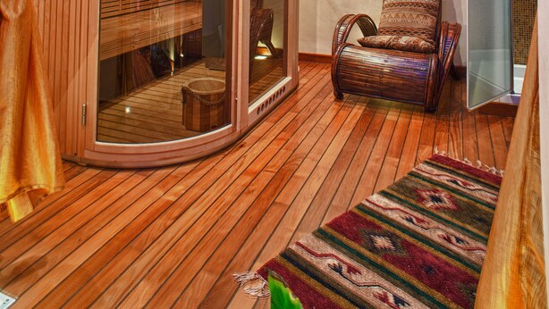 Una habitación acogedora con techo de madera, un rincón de estar con paredes de vidrio y una alfombra estampada en el suelo.