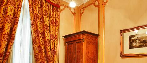 A hotel room with a red carpet, a wooden wardrobe, a bed with a yellow bedspread, a red armchair, and a chandelier.