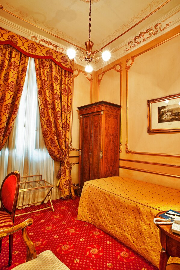 A hotel room with a red carpet, a wooden wardrobe, a bed with a yellow bedspread, a red armchair, and a chandelier. - Grand Hotel Wagner (Palermo)