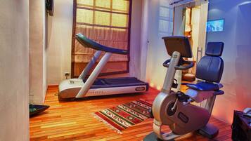 Una habitación pequeña con una cinta de correr, una bicicleta estática y un televisor en la pared.