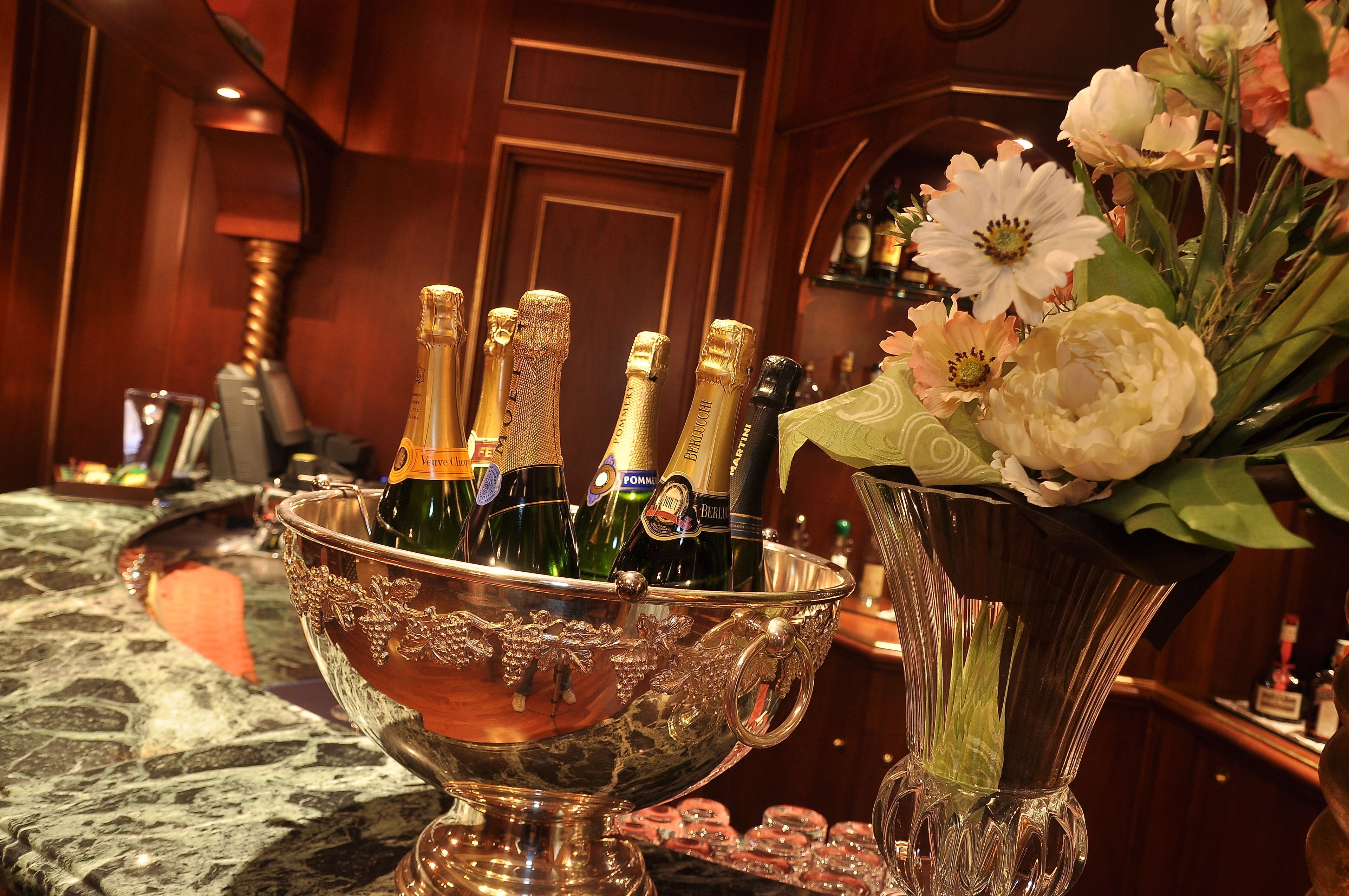 A bar area with a large silver bowl containing champagne bottles, a vase with flowers, and a marble countertop.