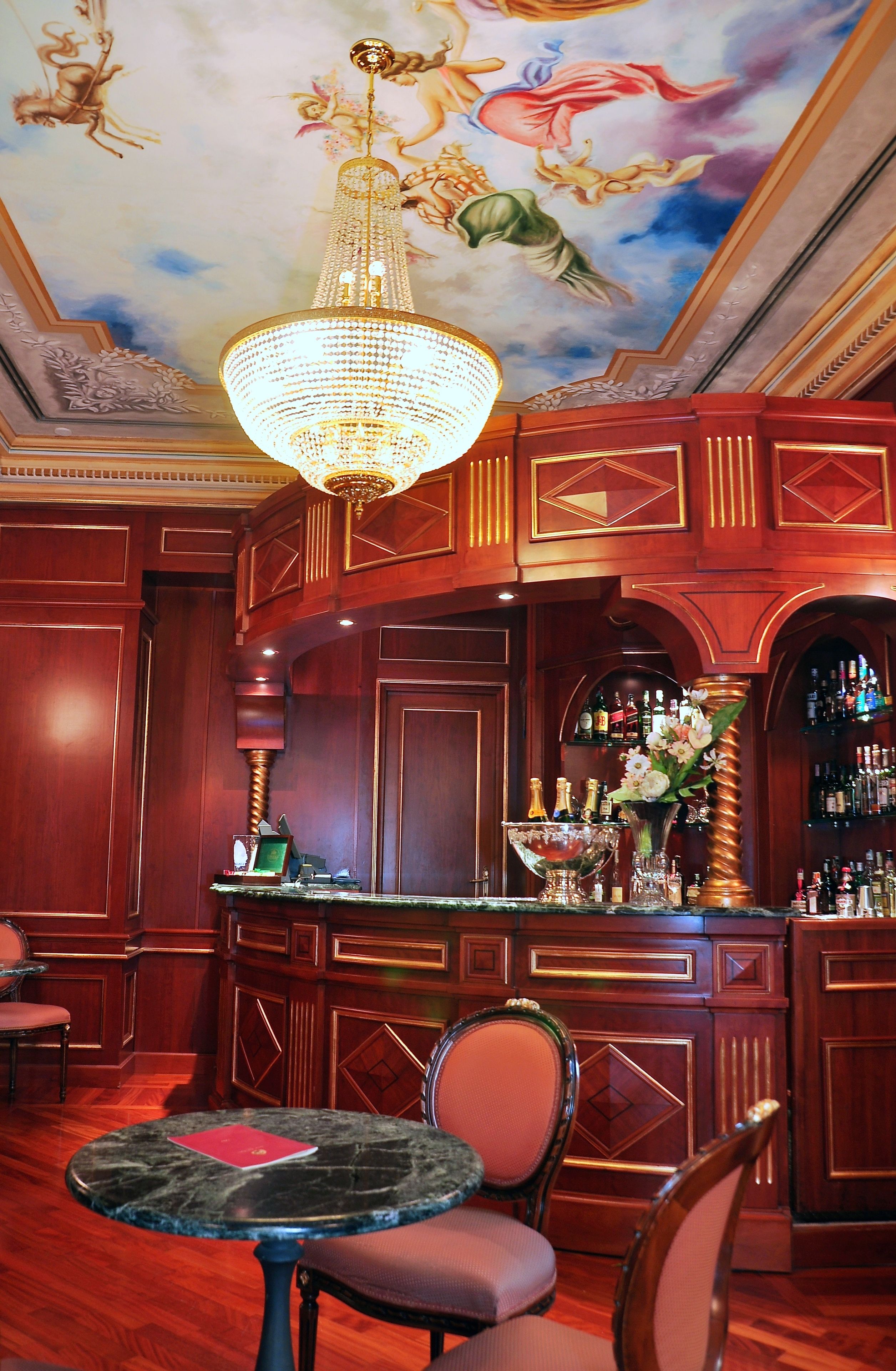 A bar area with a chandelier, wooden paneling, a bar counter, and a seating area with a table and chairs.