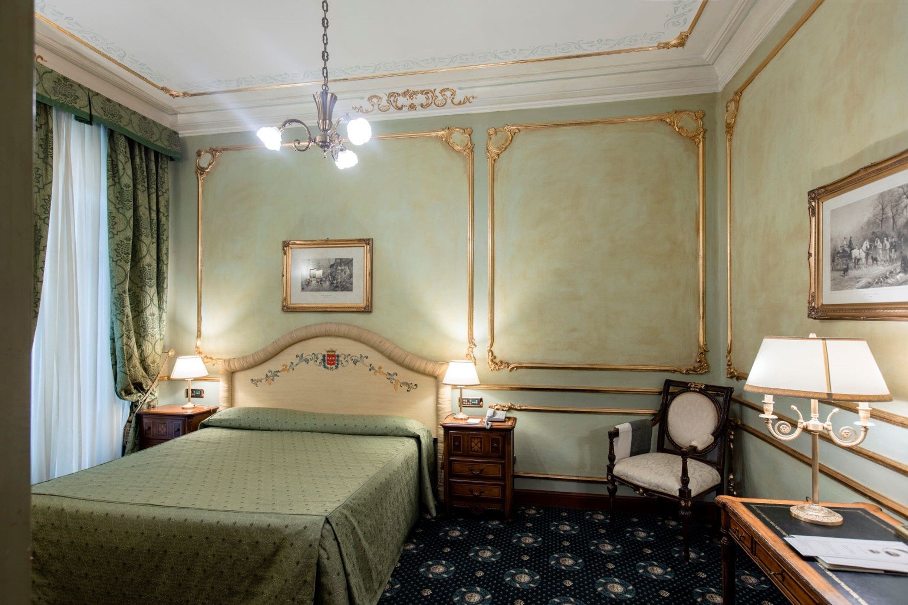 Ein Hotelzimmer mit Bett, Sessel, Schreibtisch und einer Kandelaber.