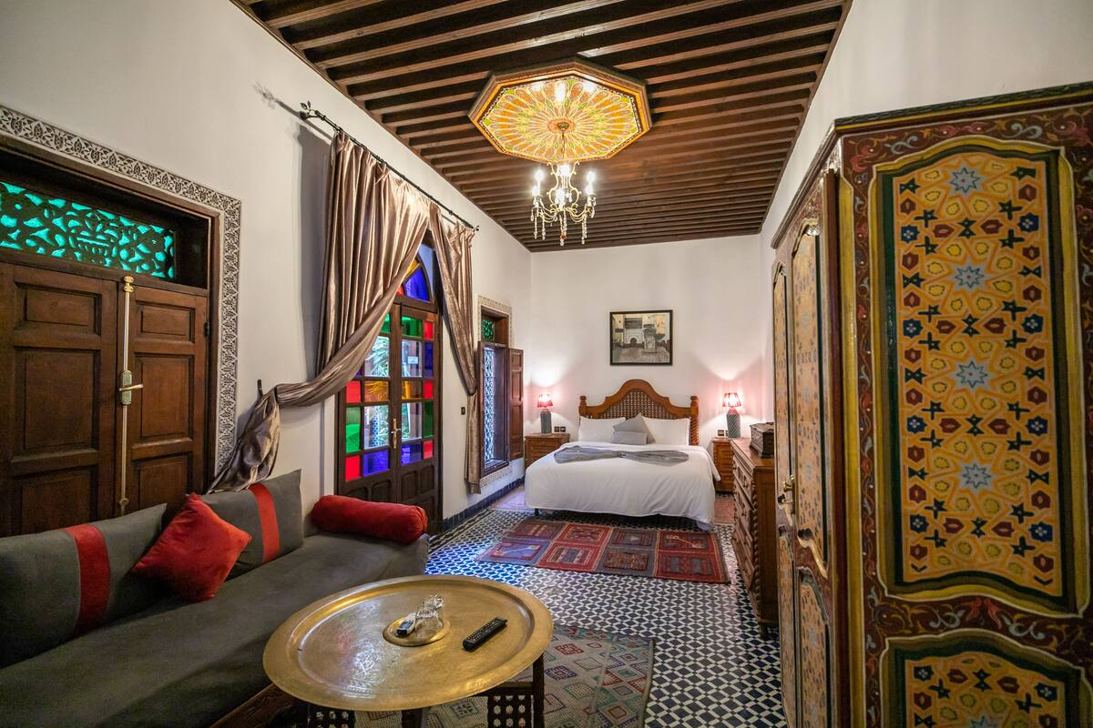 A traditional room with a bed, a sofa, a small table, and a patterned floor.