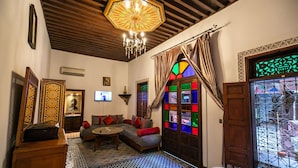 A cozy room with a wooden ceiling, a patterned floor, a sofa with cushions, a small table, and a decorative door with a stained glass window. - Riad dar Chrifa (Fes)