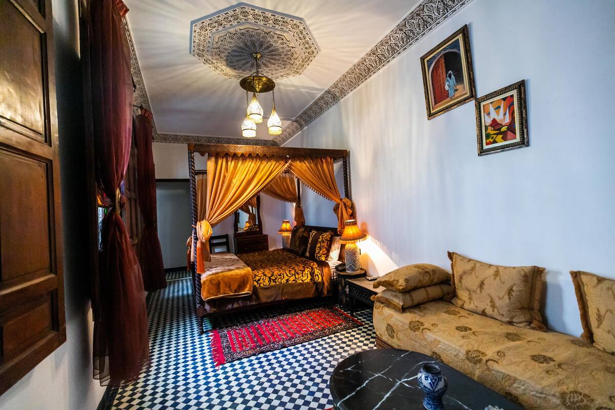 A traditional room with a checkered floor, a four-poster bed, a sofa, and a patterned ceiling.
