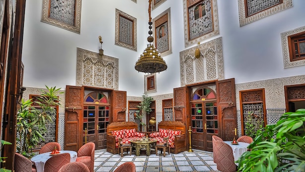 A traditional Moroccan interior with ornate tile work, a central seating area, and a hanging chandelier. - Riad dar Chrifa (Fes)