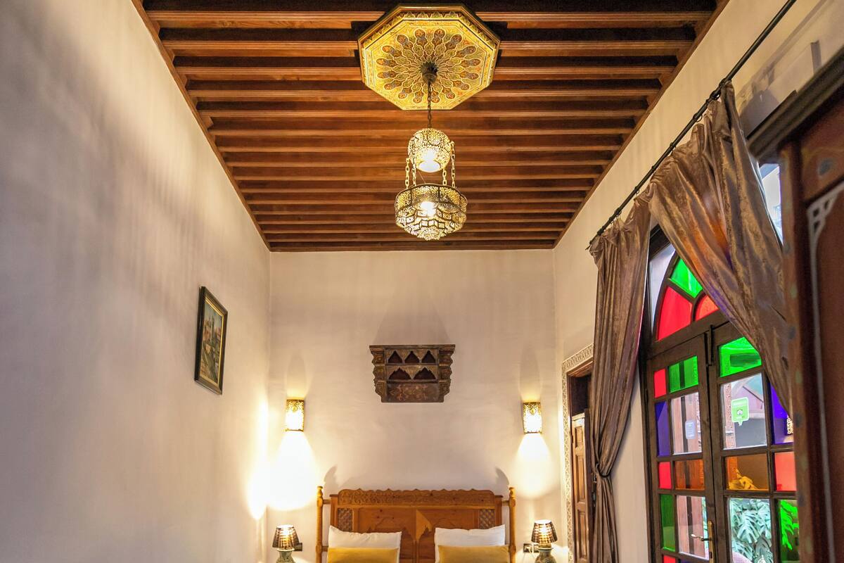 A room with two beds, a wooden ceiling, a patterned floor, and a stained glass window.