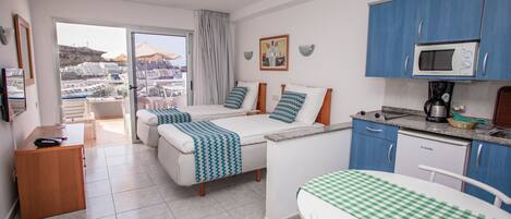 A hotel room with a balcony, a kitchenette, and a bed with a view.