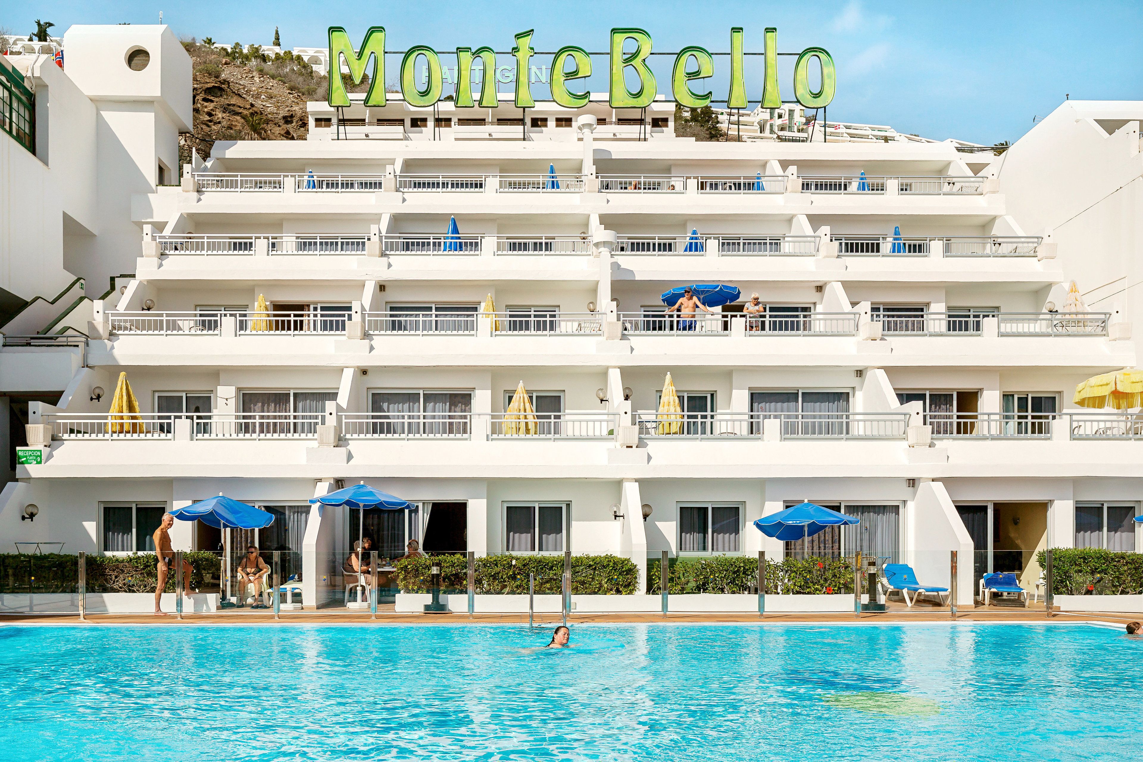 A hotel with a swimming pool, multiple balconies, and umbrellas.