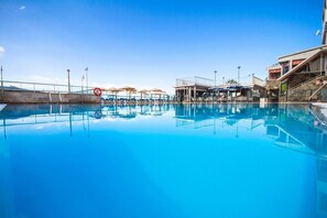 A clear blue pool with lounge chairs and umbrellas, a lifebuoy, and a building with a balcony. - Servatur Montebello (Mogan)
