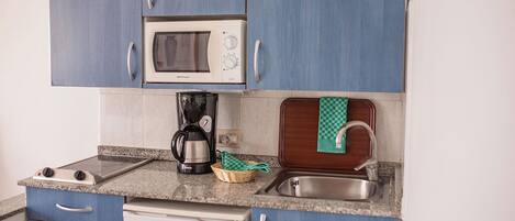 Una cocina compacta con microondas, cafetera y lavamanos con una bandeja de madera.