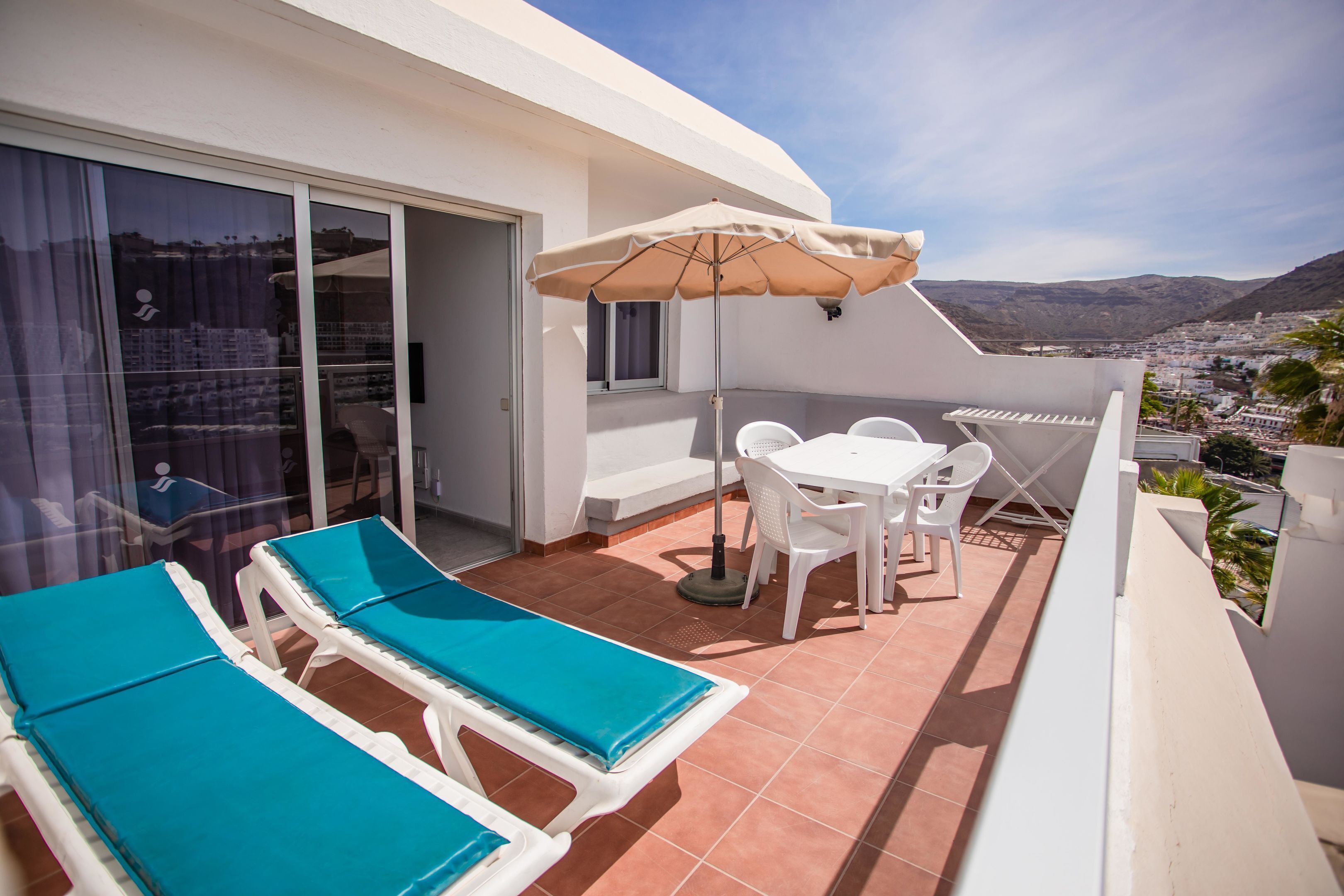 A balcony with two lounge chairs, a table, and an umbrella.