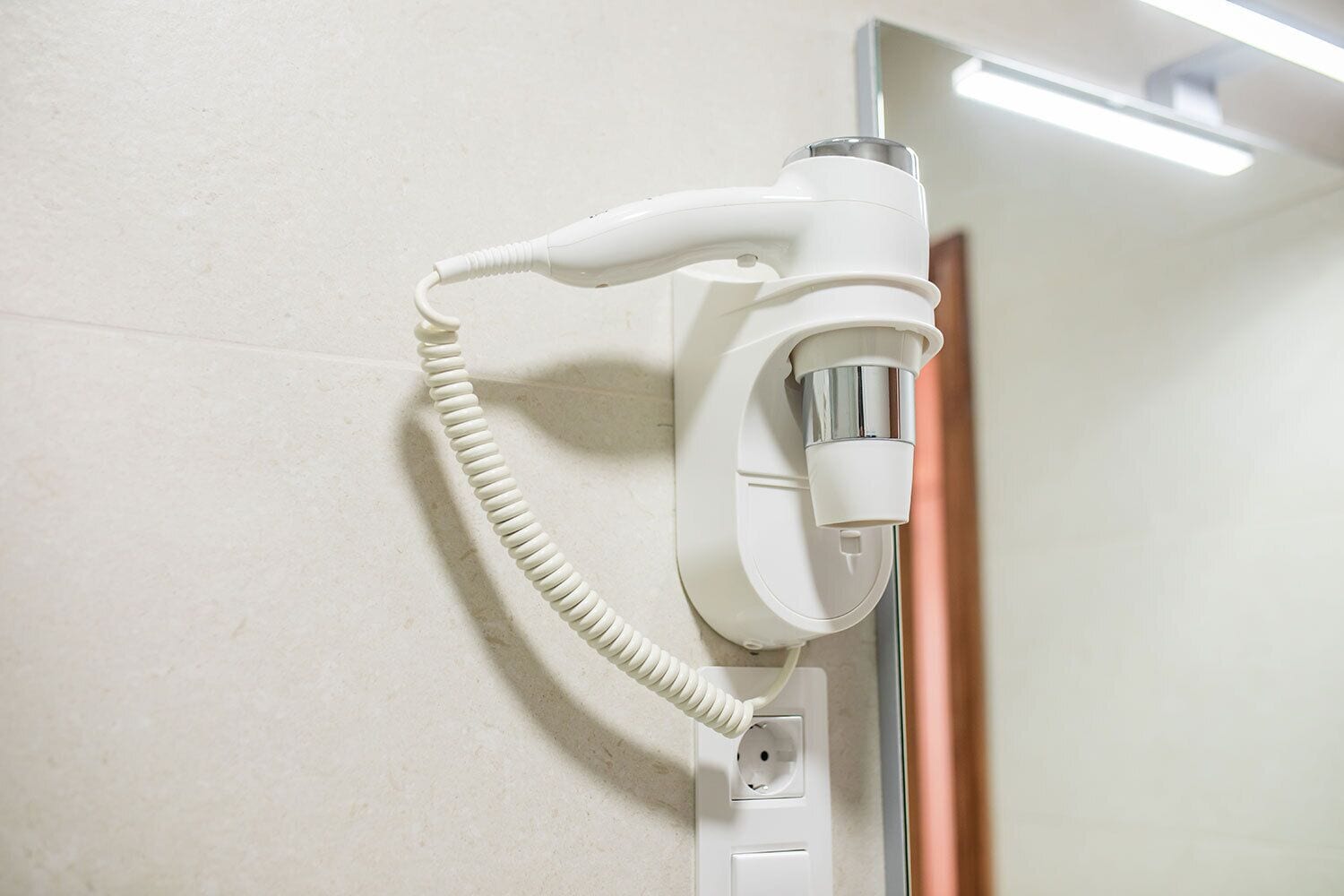 Un sèche-cheveux blanc fixé au mur, avec un cordon.