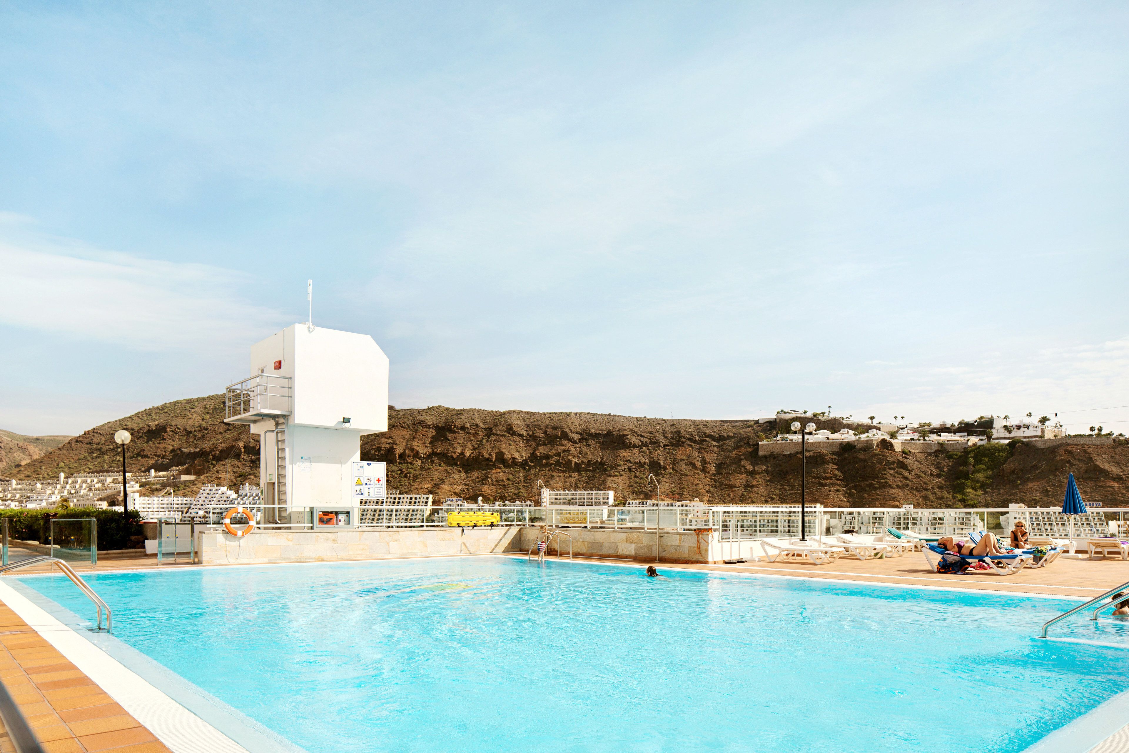 A swimming pool with a lifeguard tower, lounge chairs, and a view of a hillside.