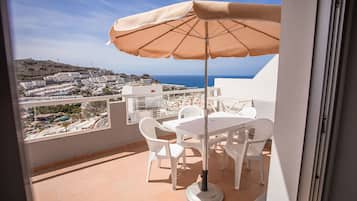 Un balcón con mesa y sillas, una sombrilla color beige y vista a un pueblo costero.