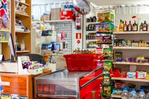 A small grocery store with shelves stocked with various products, a cash register, and a red shopping basket. - Servatur Montebello (Mogan)