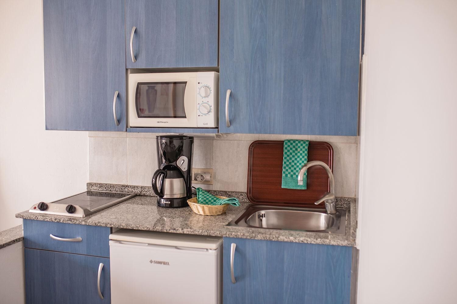 Uma cozinha compacta com micro-ondas, cafeteira e pia com toalha xadrez.
