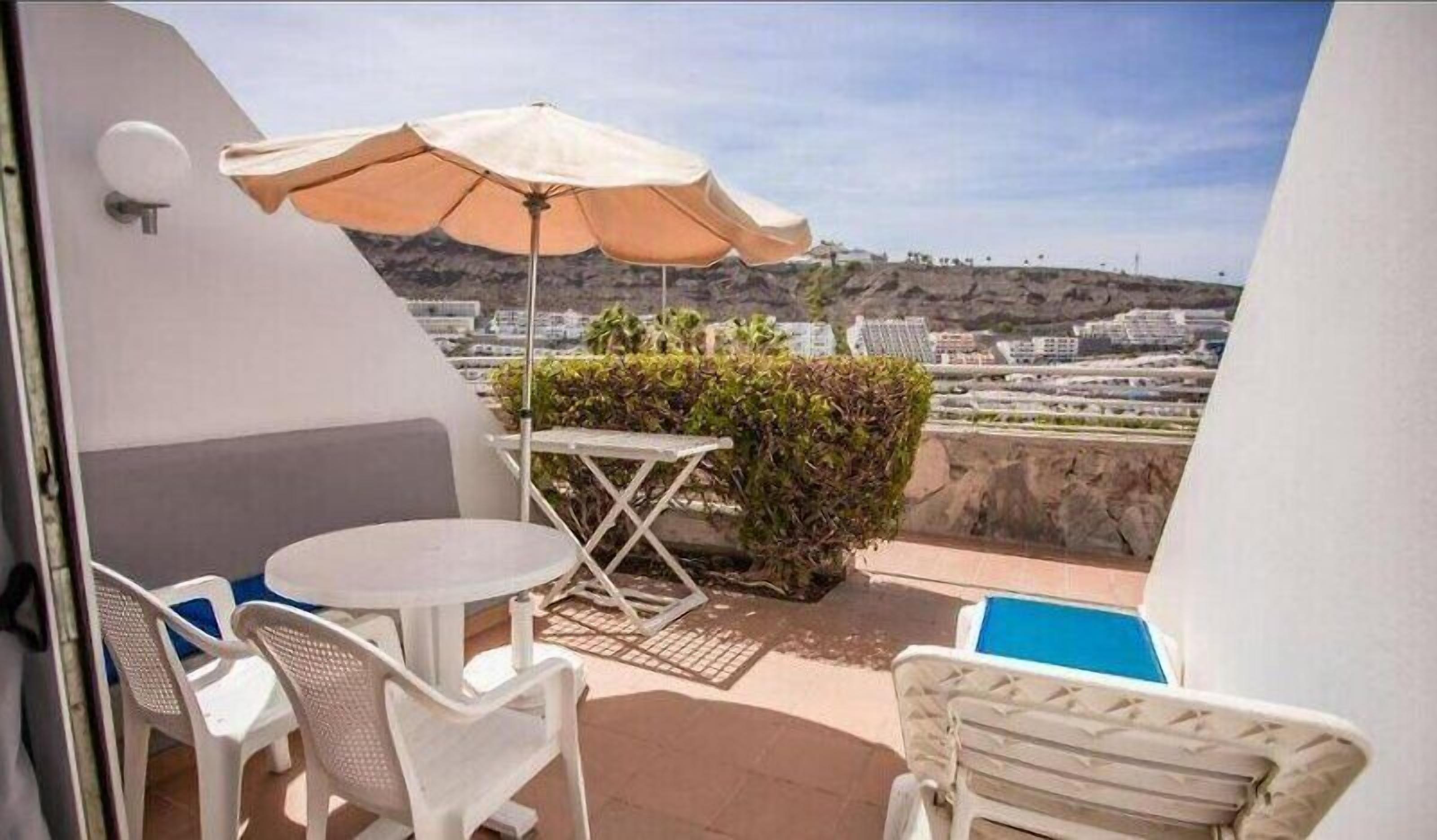 A balcony with a table and chairs, an umbrella, and a view of the cityscape.