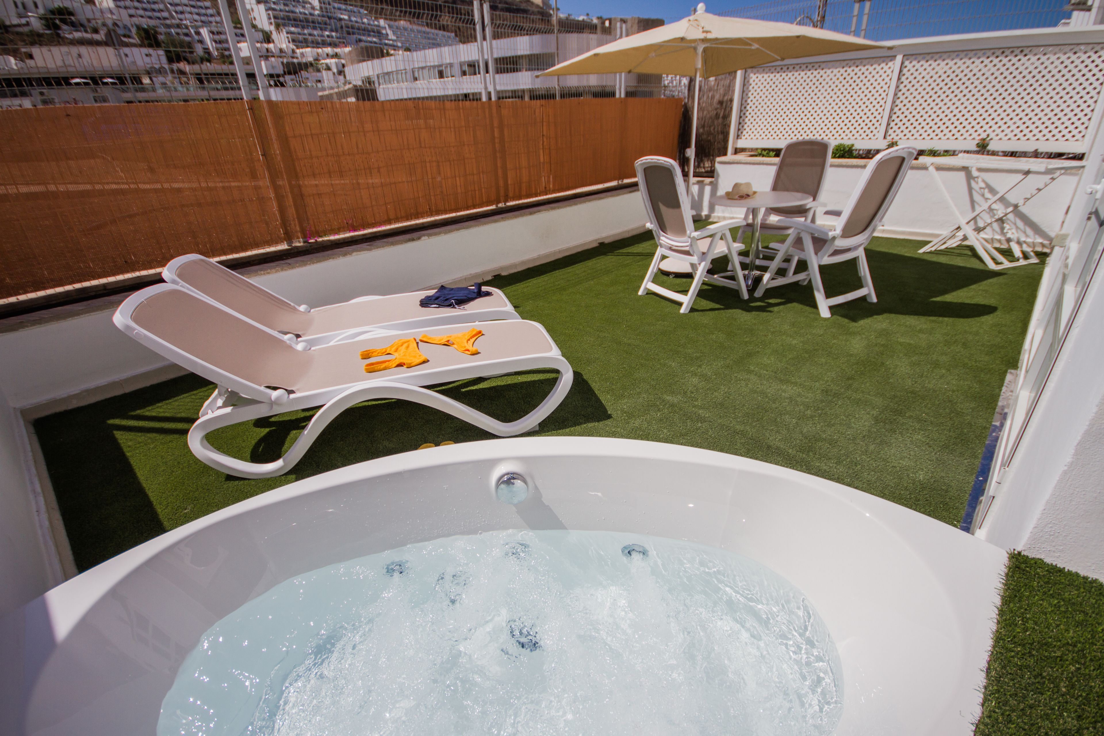 Terraza en la azotea con jacuzzi, sillones de descanso y una mesa con sillas.
