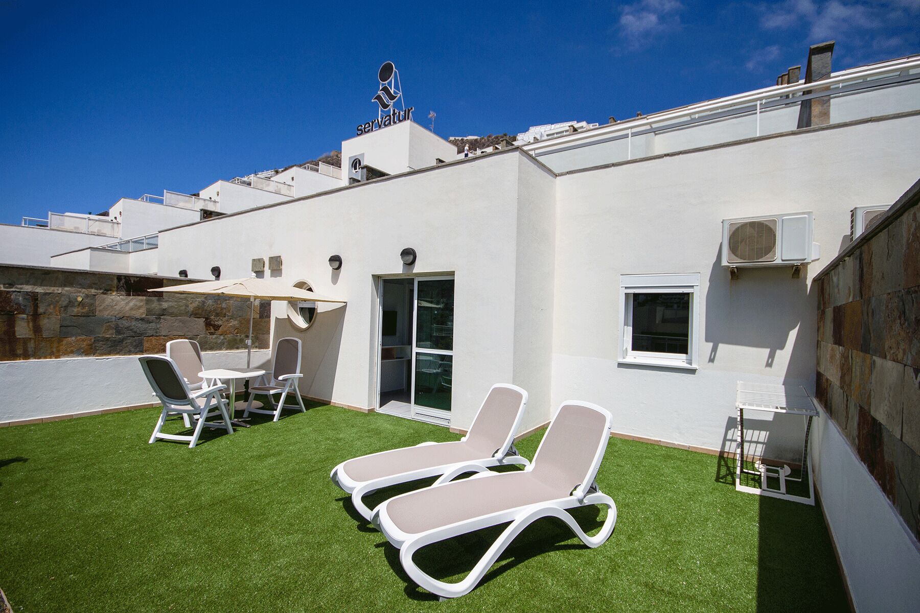 Terraza en la azotea con dos sillones, una mesa y una sombrilla.