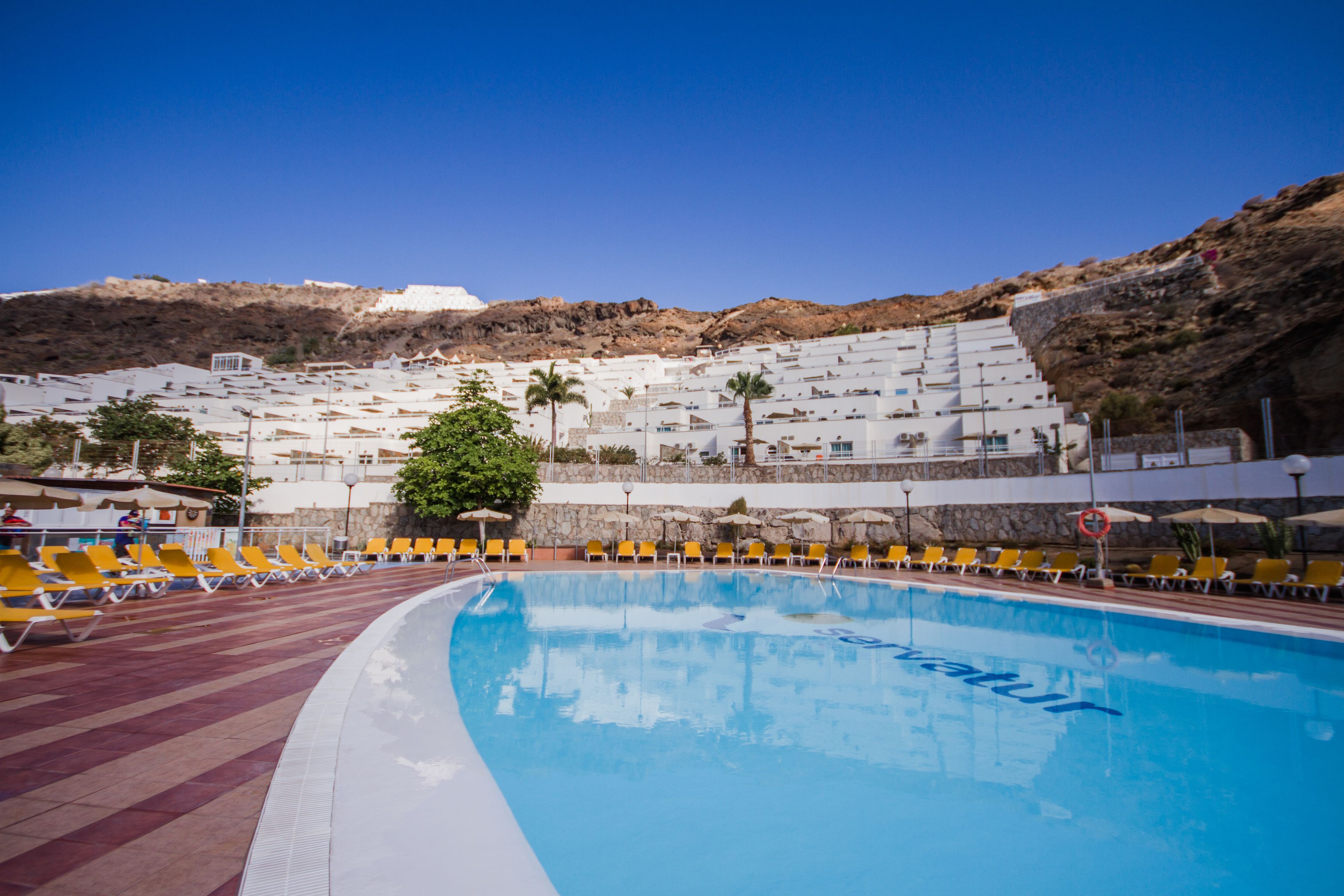Une piscine avec des chaises longues jaunes et un bâtiment blanc en arrière-plan.