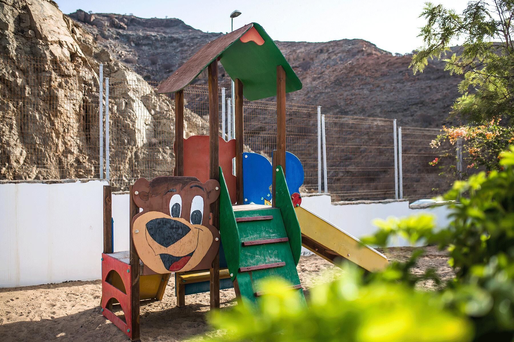 Une aire de jeux pour enfants avec un motif d’ours, un toboggan et une zone d’escalade, le tout installé sur une colline rocheuse.